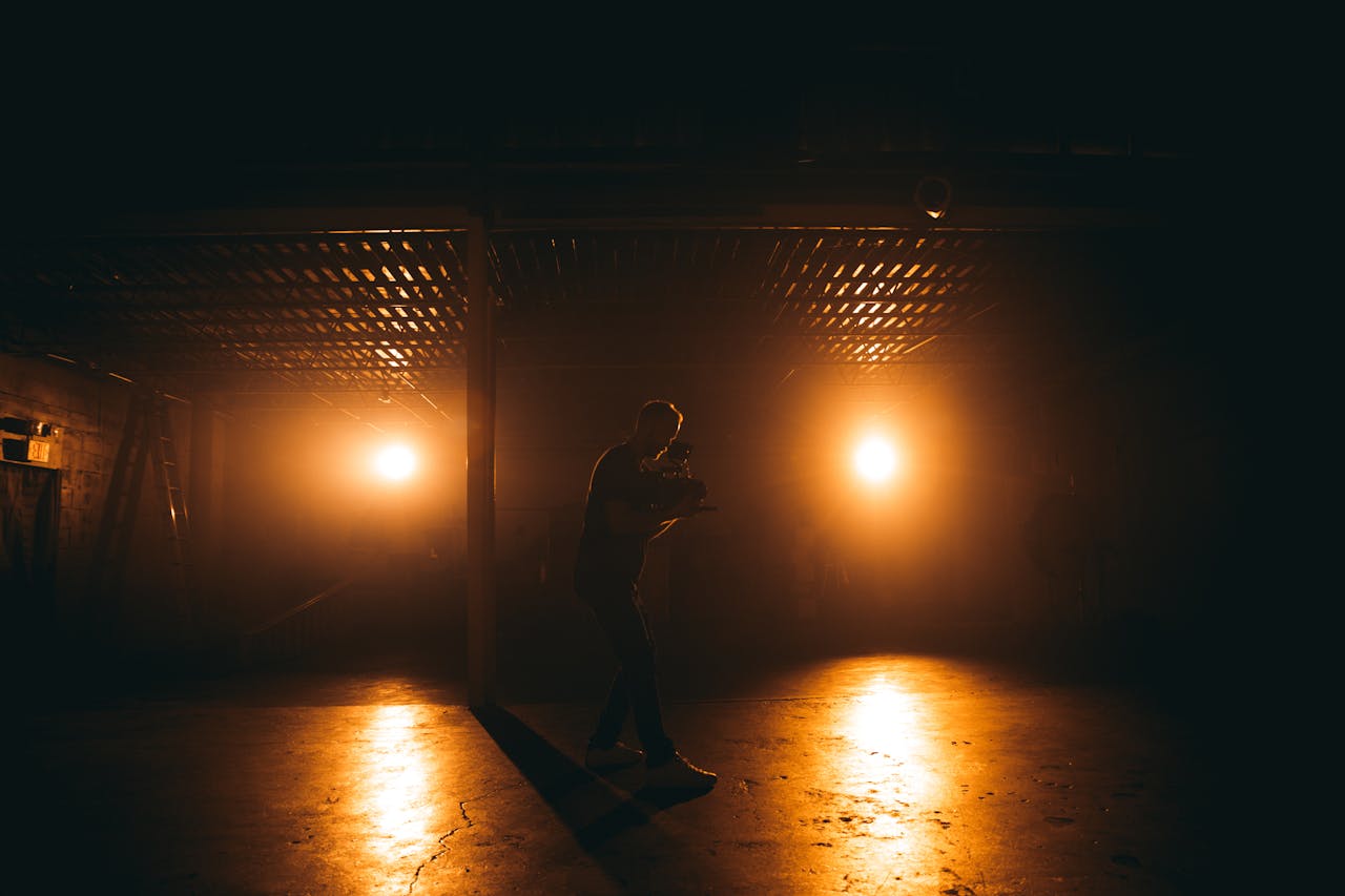A silhouetted man filming with professional equipment under dramatic lighting in a dim setting.